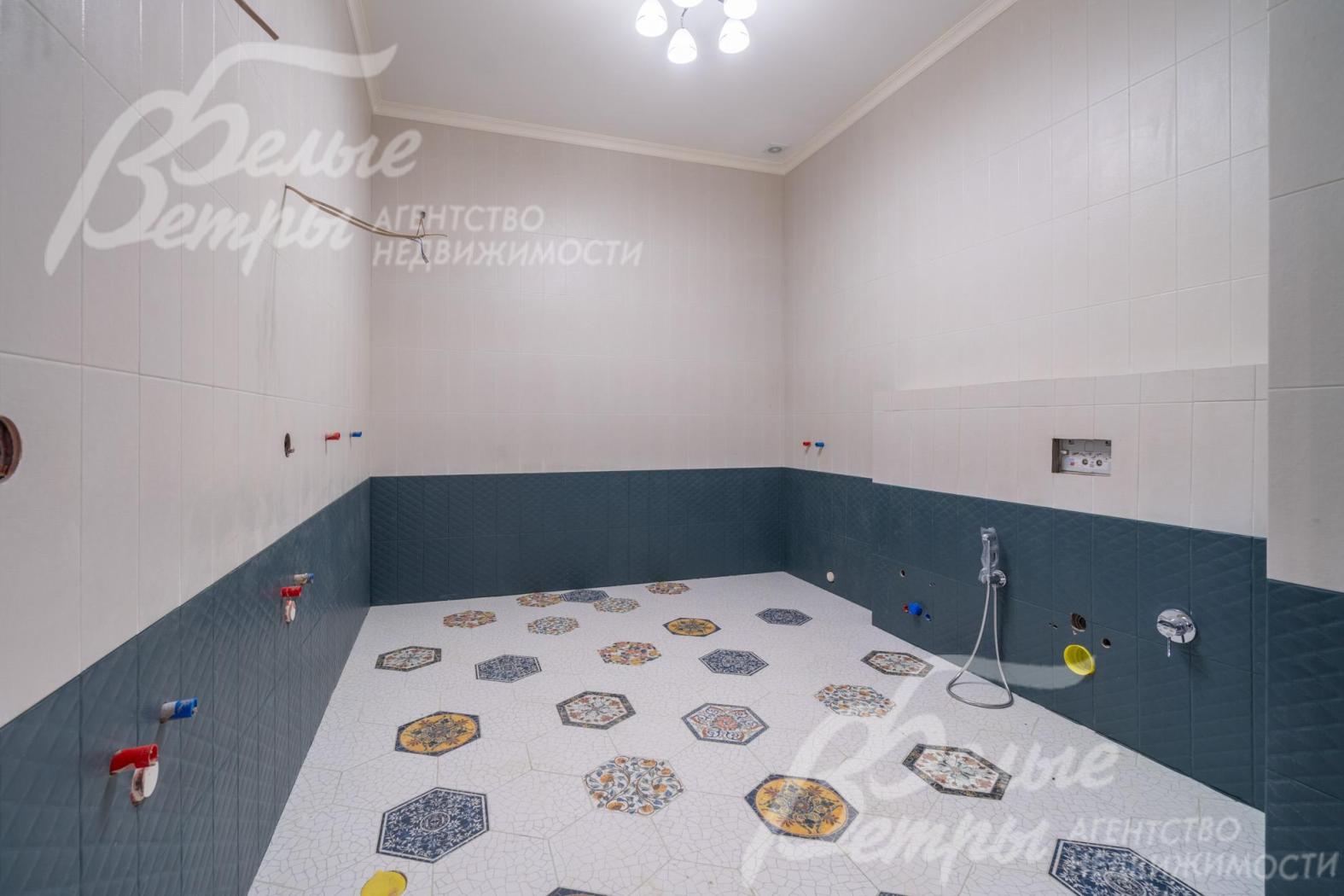 Один из санузлом. Нижняя часть стен облицована тёмно-серой плиткой, верхняя — в молочном нейтральном оттенке, пол украшен плиткой с геометрическим узором