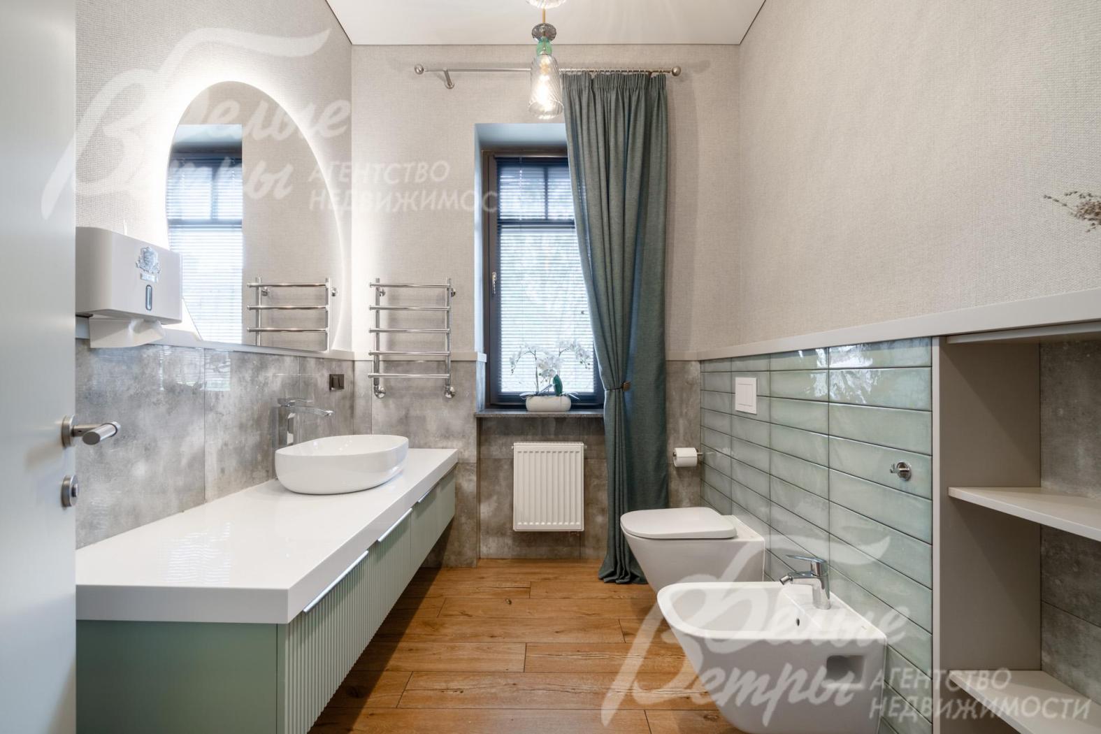 В стильно оформленном санузле первого этажа - овальная раковина на длинной столешнице, зеркало с подсветкой, унитаз и биде