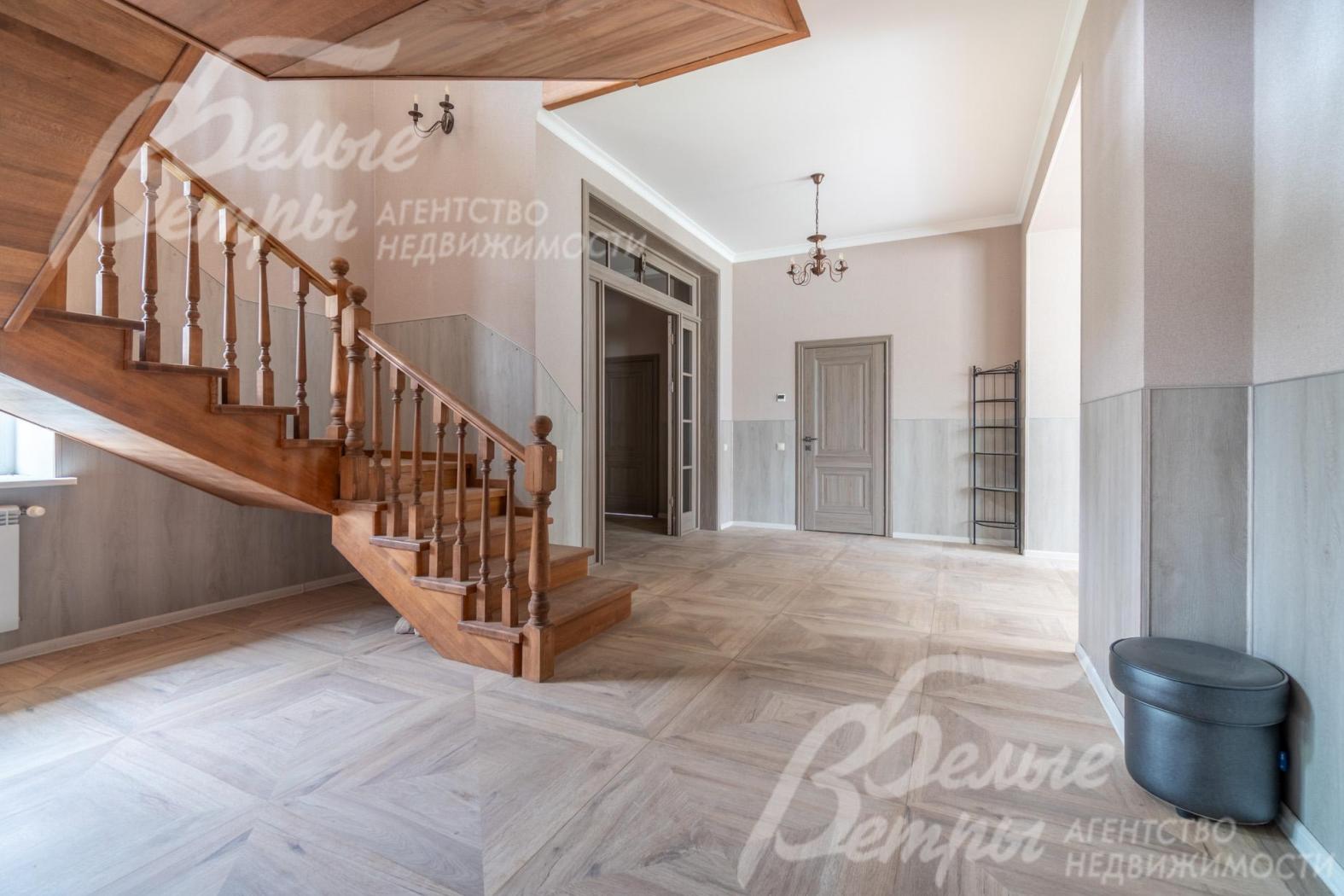 Холл на первом этаже с раздвижной дверью-порталом в столовую-гостиную и эффектной лестницей из дерева