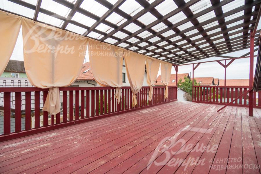 Крытая терраса на первом этаже - с полом из досок, окрашенных в насыщенный бордовый цвет и ограждением из деревянных балясин того же оттенка