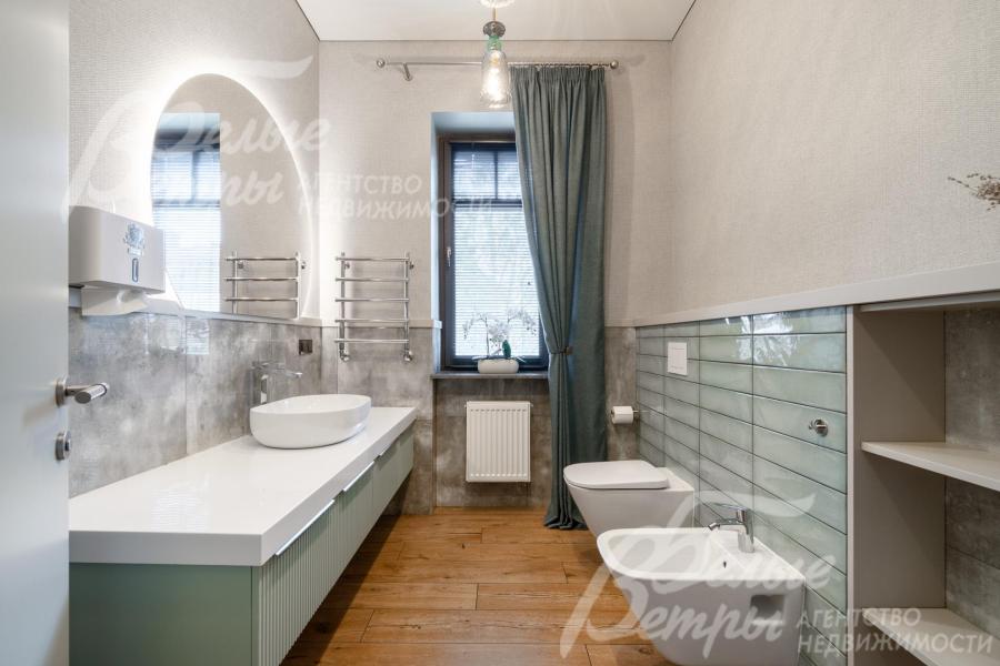 В стильно оформленном санузле первого этажа - овальная раковина на длинной столешнице, зеркало с подсветкой, унитаз и биде