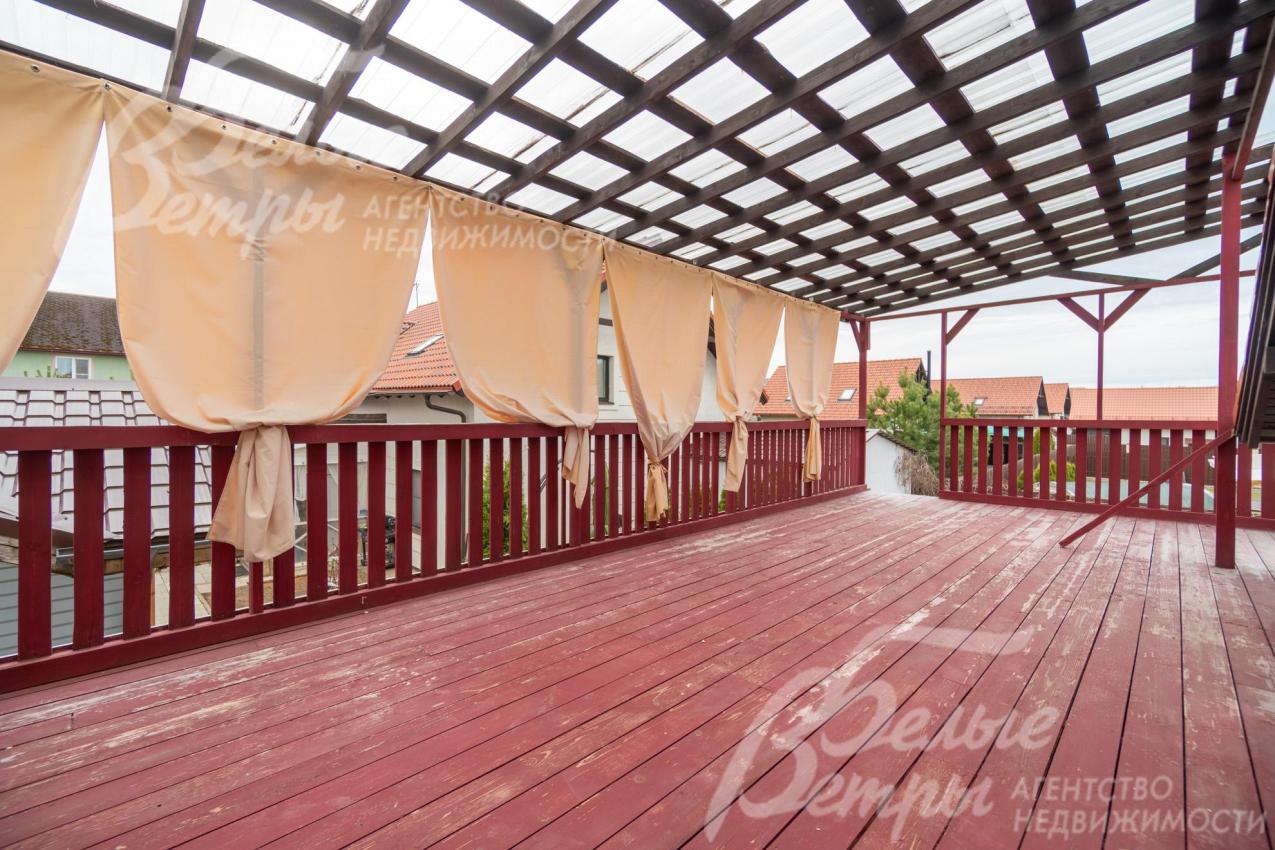 Крытая терраса на первом этаже - с полом из досок, окрашенных в насыщенный бордовый цвет и ограждением из деревянных балясин того же оттенка