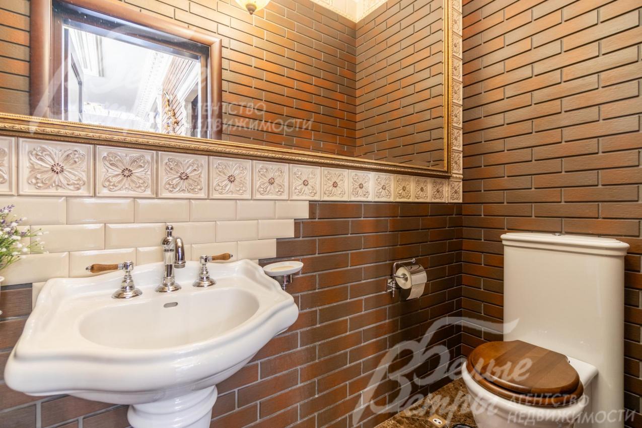 Гостевой санузел на первом этаже с большим зеркалом, стены отделаны клинкерной плиткой
